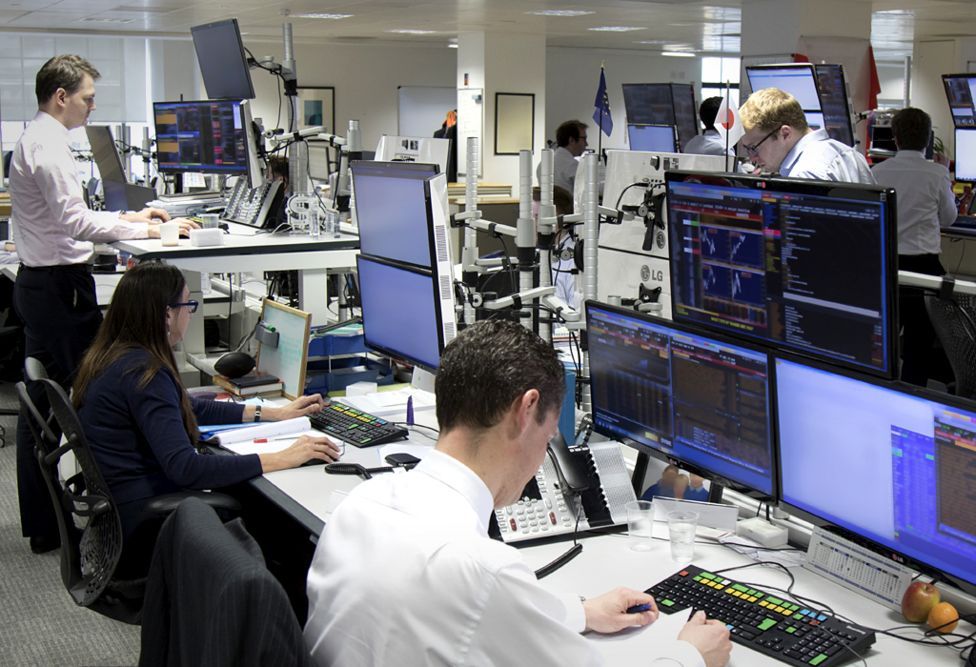 Trading floor with multiple professionals working on computers with financial data displays